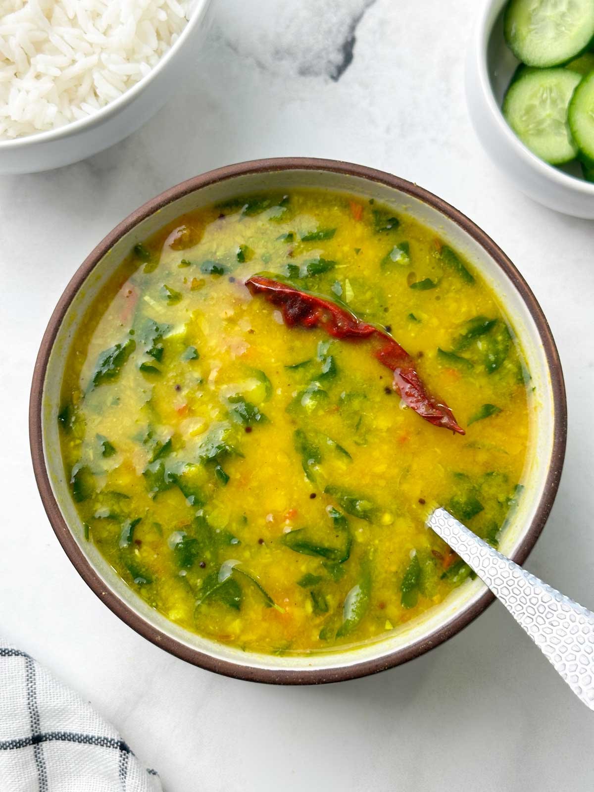 fenugreek (methi) leaves dal with a spoon served in a bowl with rice and cucumber on the side