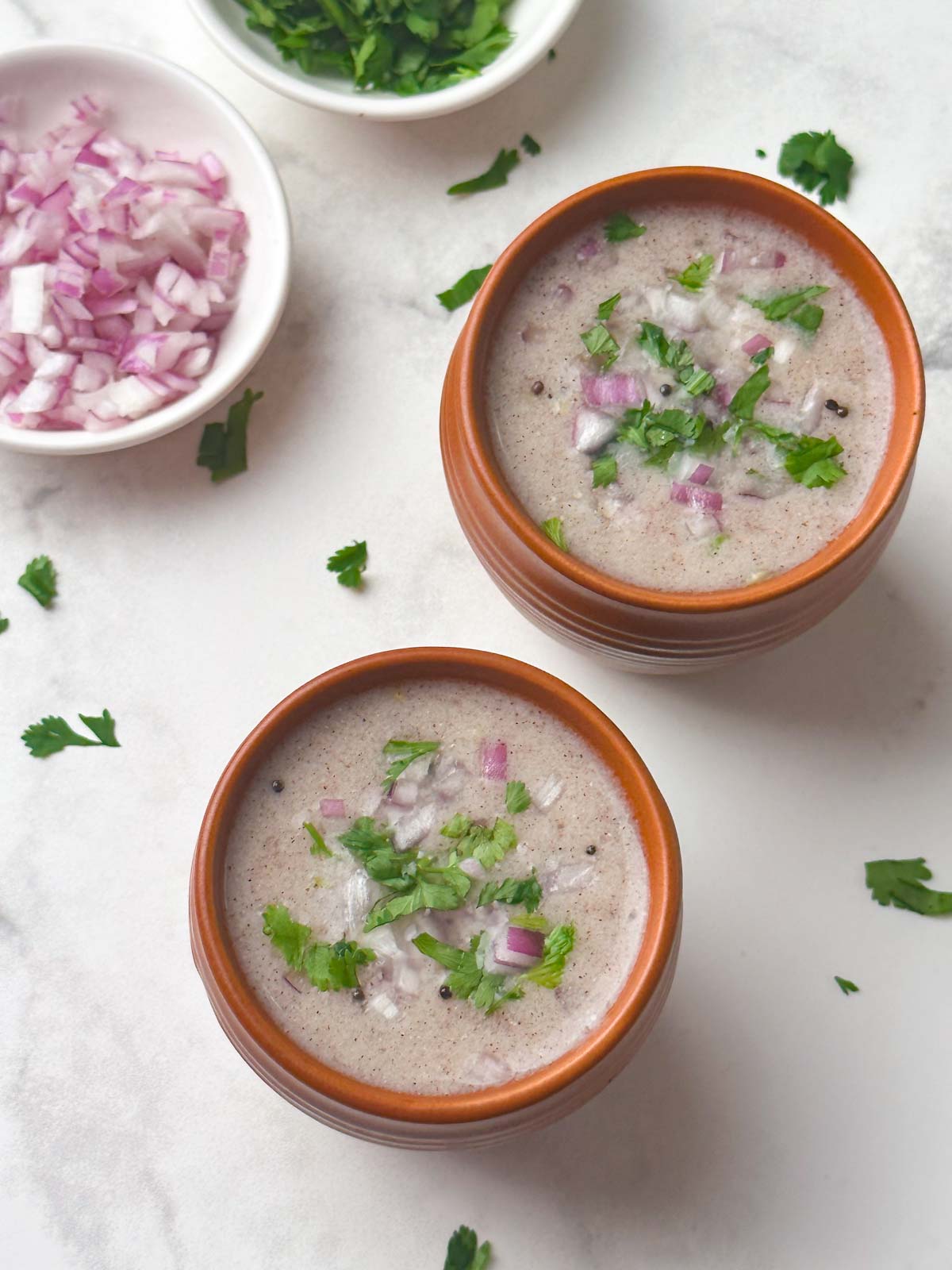 ragi ambali served in serving glasses garnished with onions and coriander