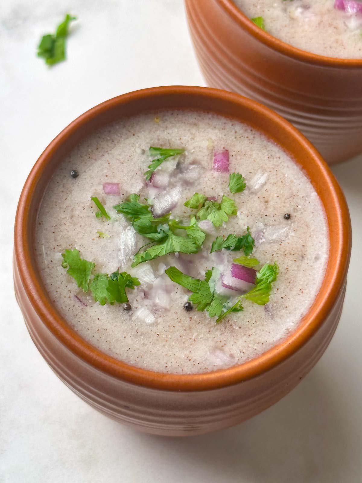 ragi ambali (ragi ganji) served in bowls with coriander and onion on the side