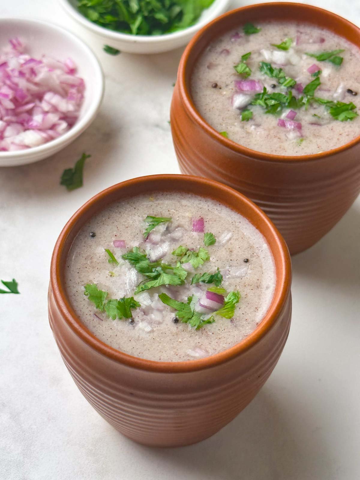 ragi ambli (ragi ganji) served in bowls with coriander and onion on the side
