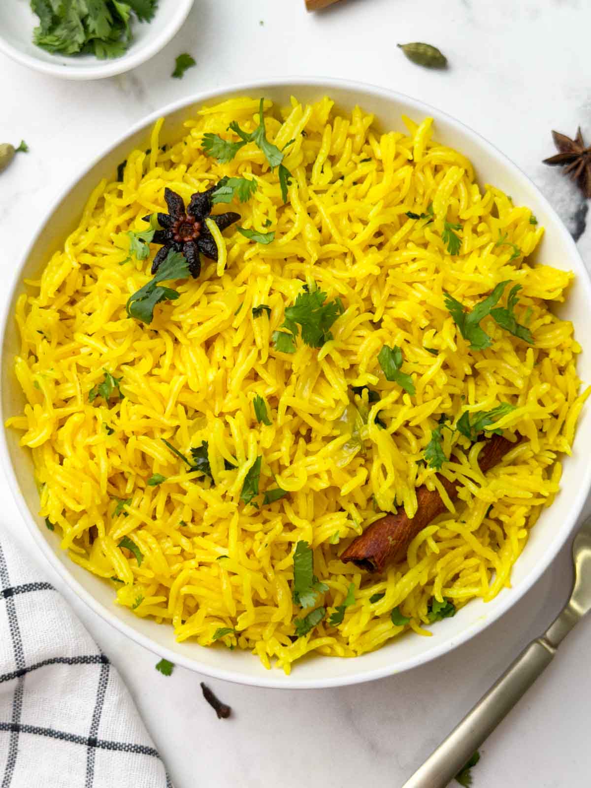 indian turmeric rice serve din a white bowl with spoon on the side