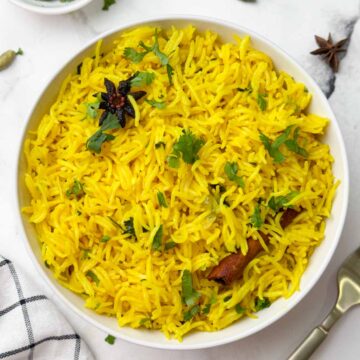 indian turmeric rice serve din a white bowl with spoon on the side