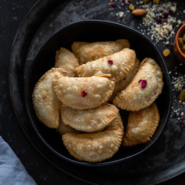 Gujiya served in a bowl with chopped nuts on the side