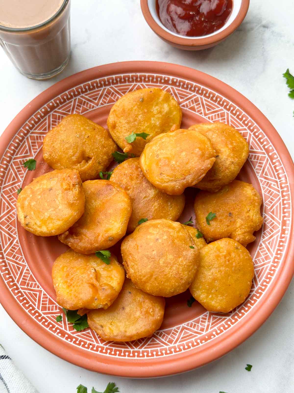 aloo pakora in a plate with tea and ketchup on the side