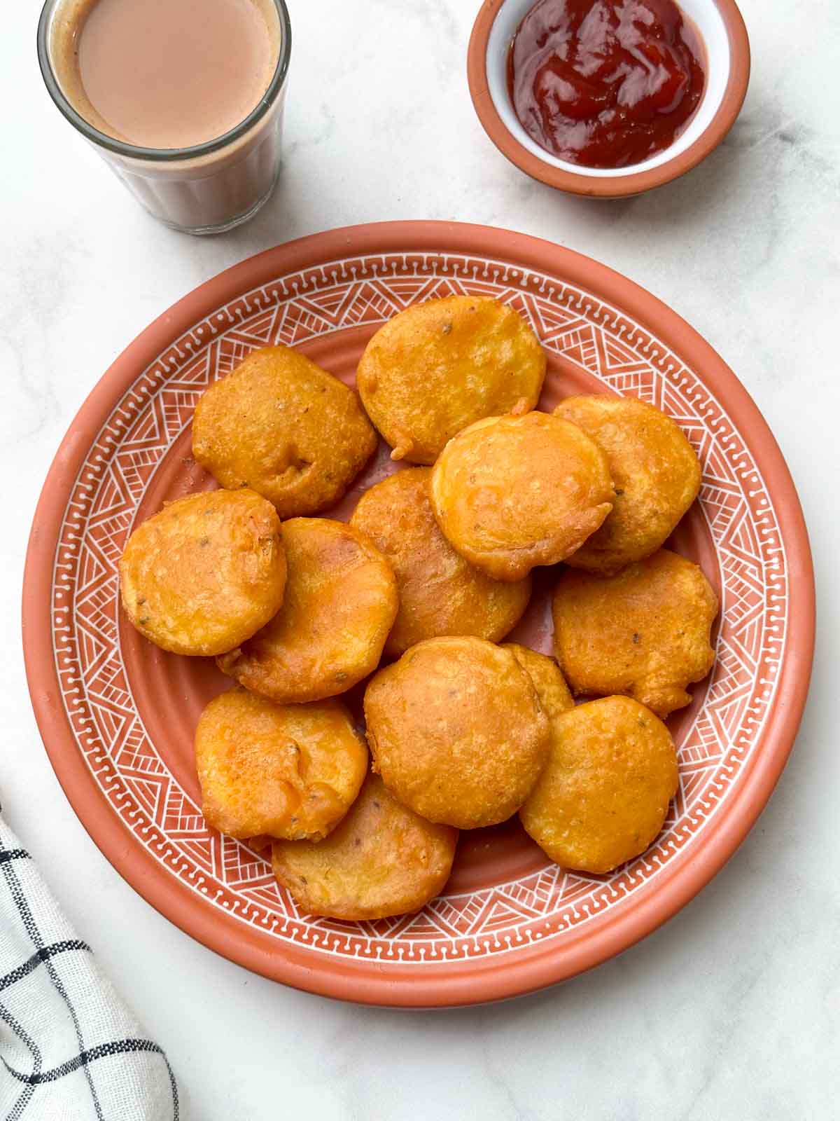 bajjis in a plate with tea and ketchup on the side