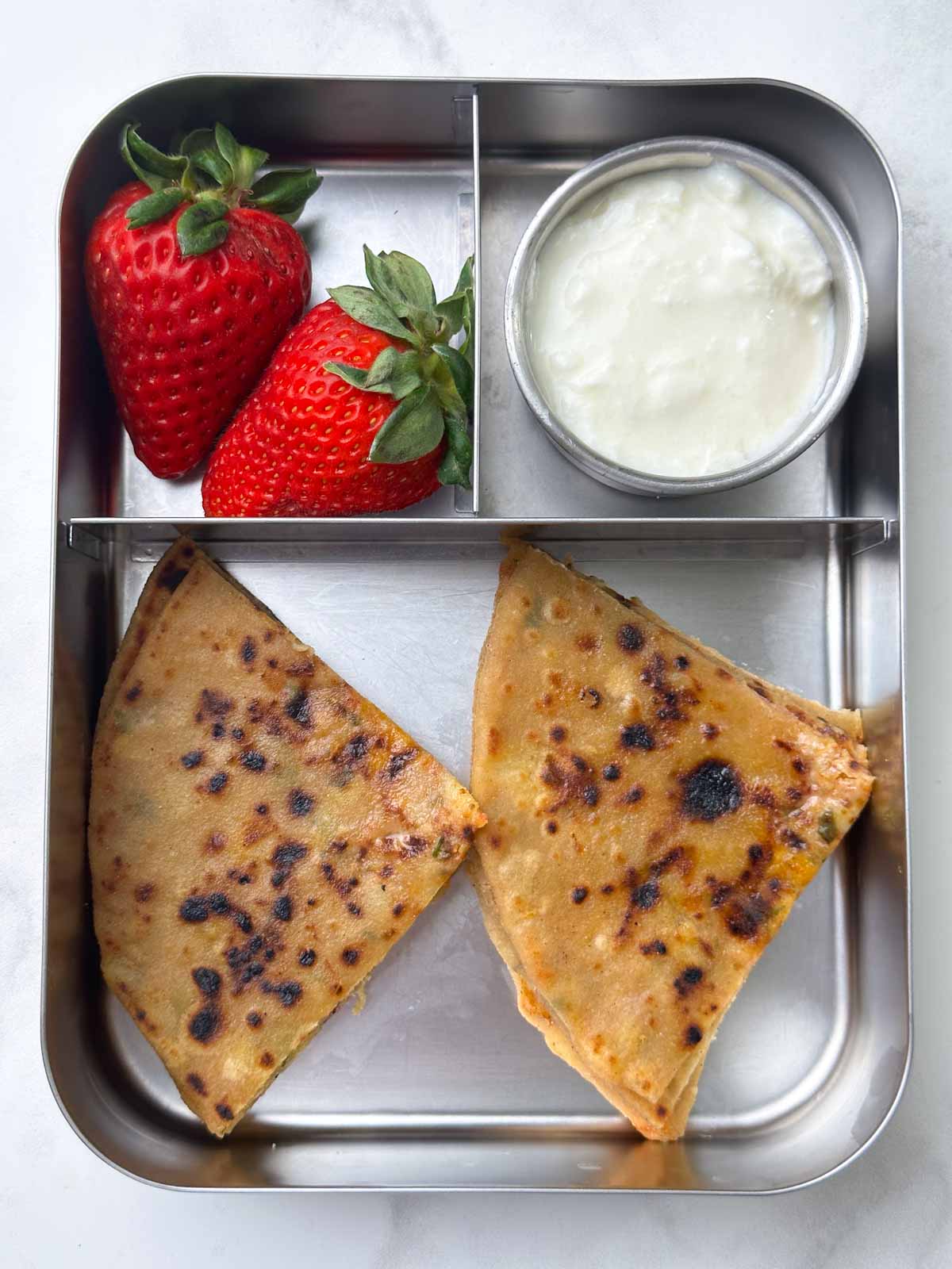 Aloo paratha with yogurt and strawberries in the steel lunch box