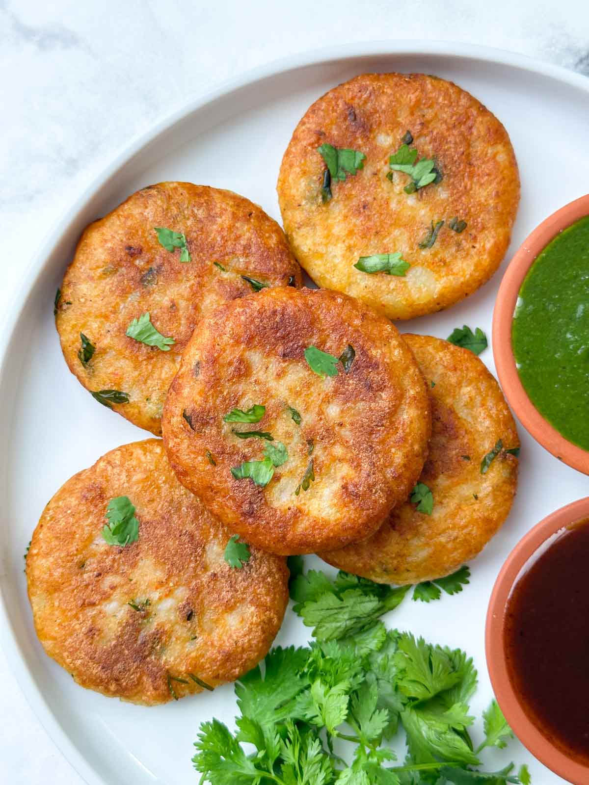 aloo tikkis served on a plate with green and tamarind chutney on the side