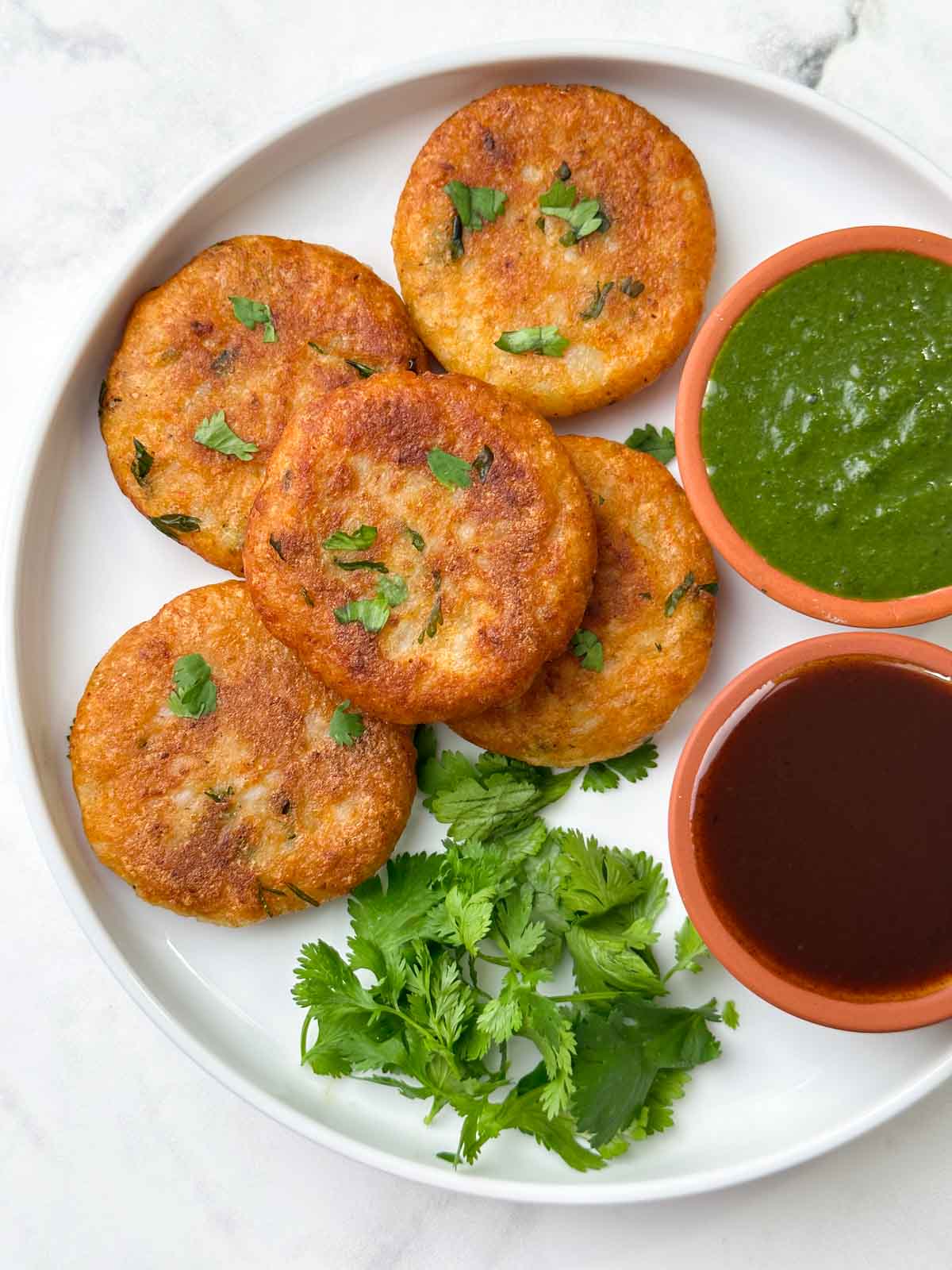 aloo tikkis served on a plate with green and tamarind chutney on the side