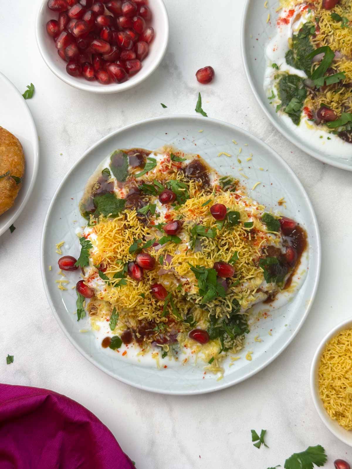 aloo tikki chaat serve don a plate with chutneys, sev and pomegranate seeds on the side