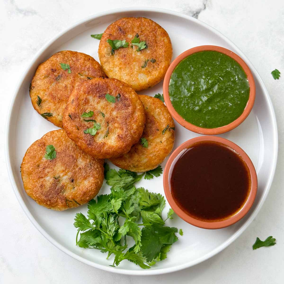 aloo tikkis served on a plate with green and tamarind chutney on the side