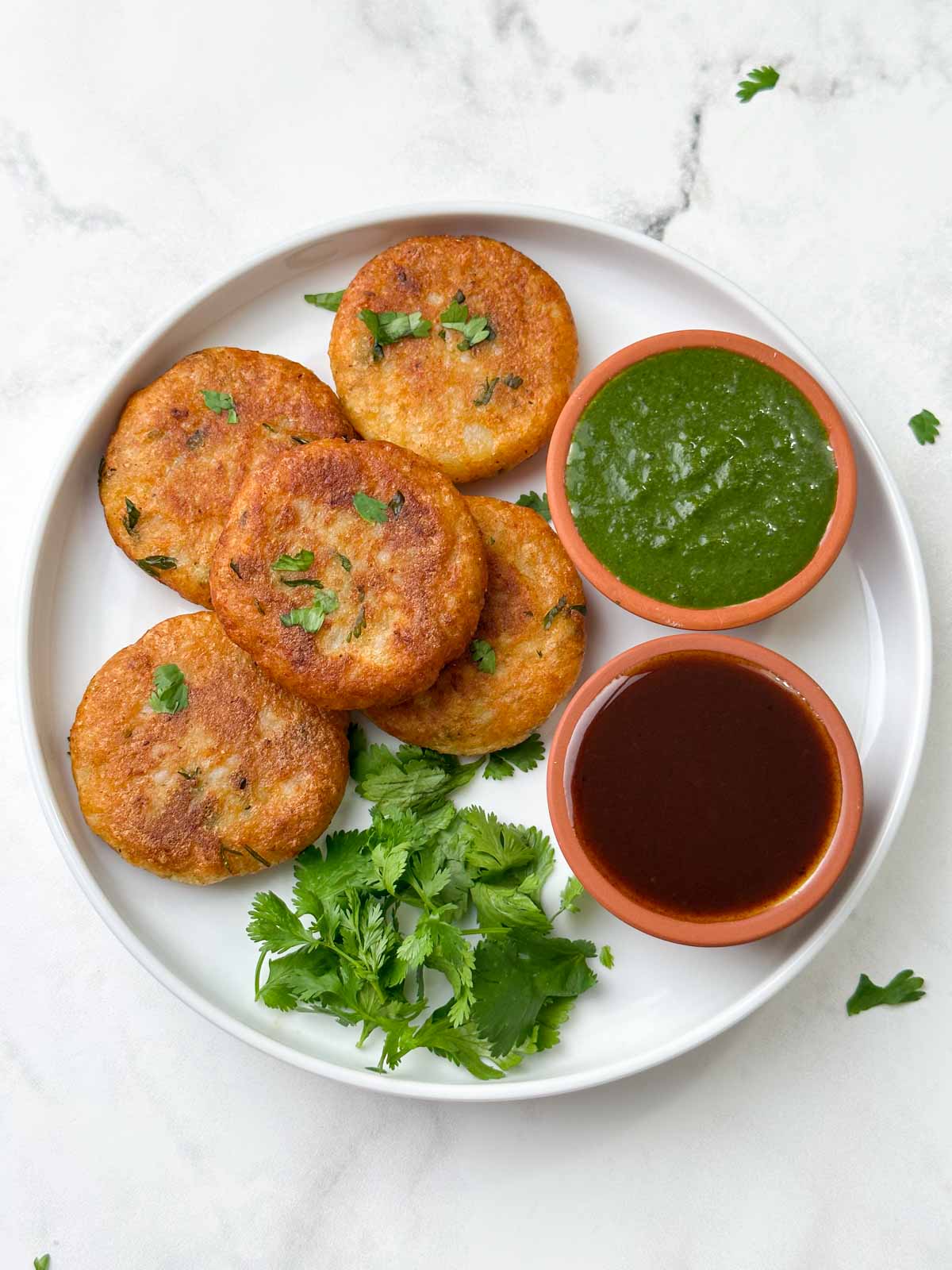 aloo tikki recipe served on a plate with green and tamarind chutney on the side