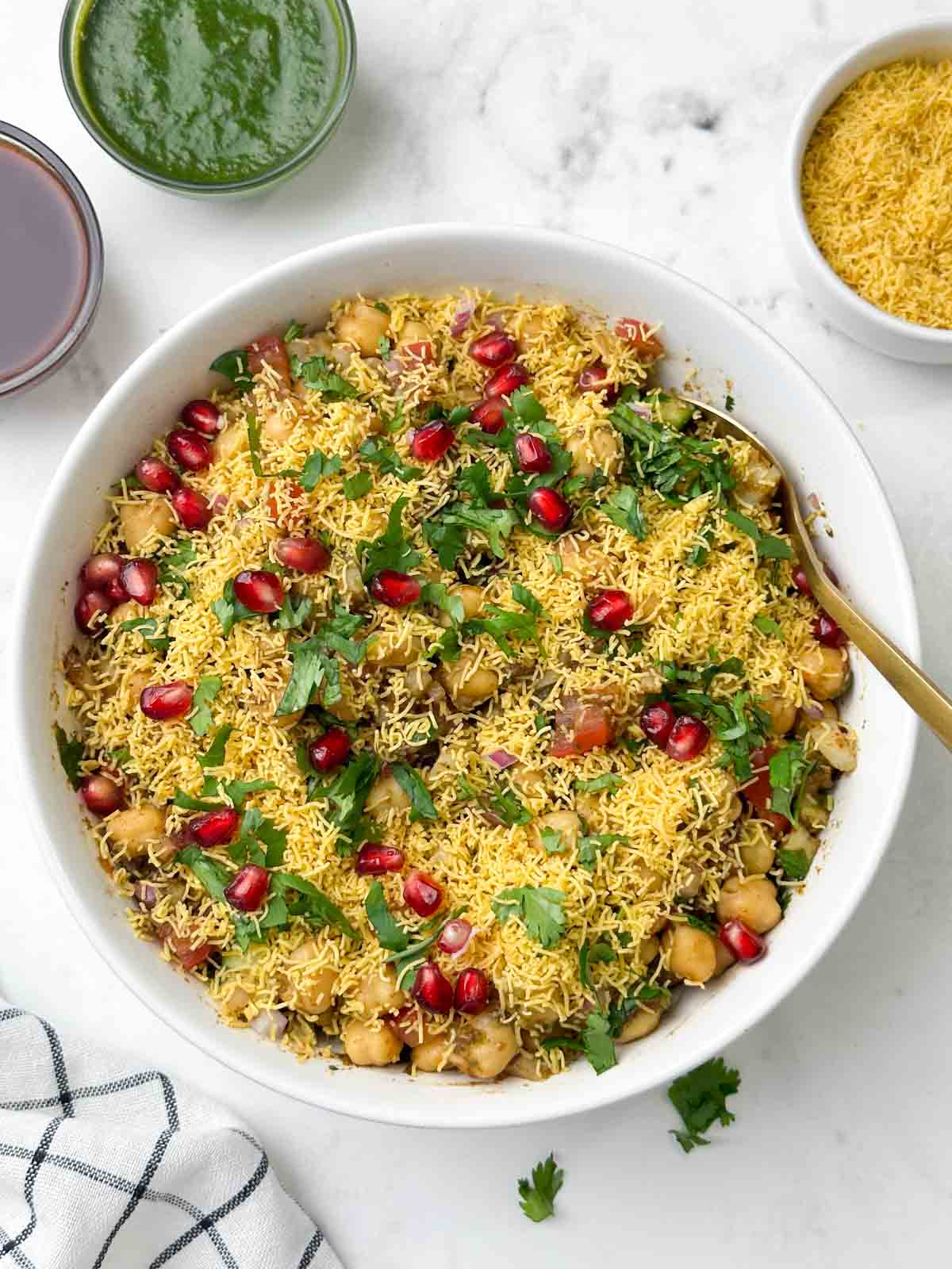 chana (chickpea) chaat served in a bowl with a spoon and chutneys and sev on the side