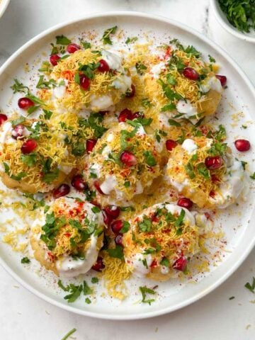 dahi puri chaat served on a plate with sev, coriander and pomegranate on the side