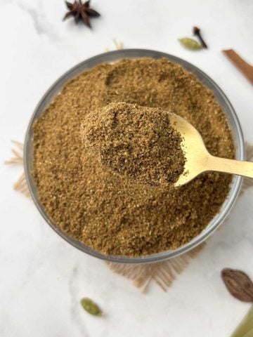 garam masala in a glass bowl and spoon full of the garam masala spice blend on the top.