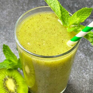 kiwi juice served in a tall glass garnished with mint leaves and straw in it.
