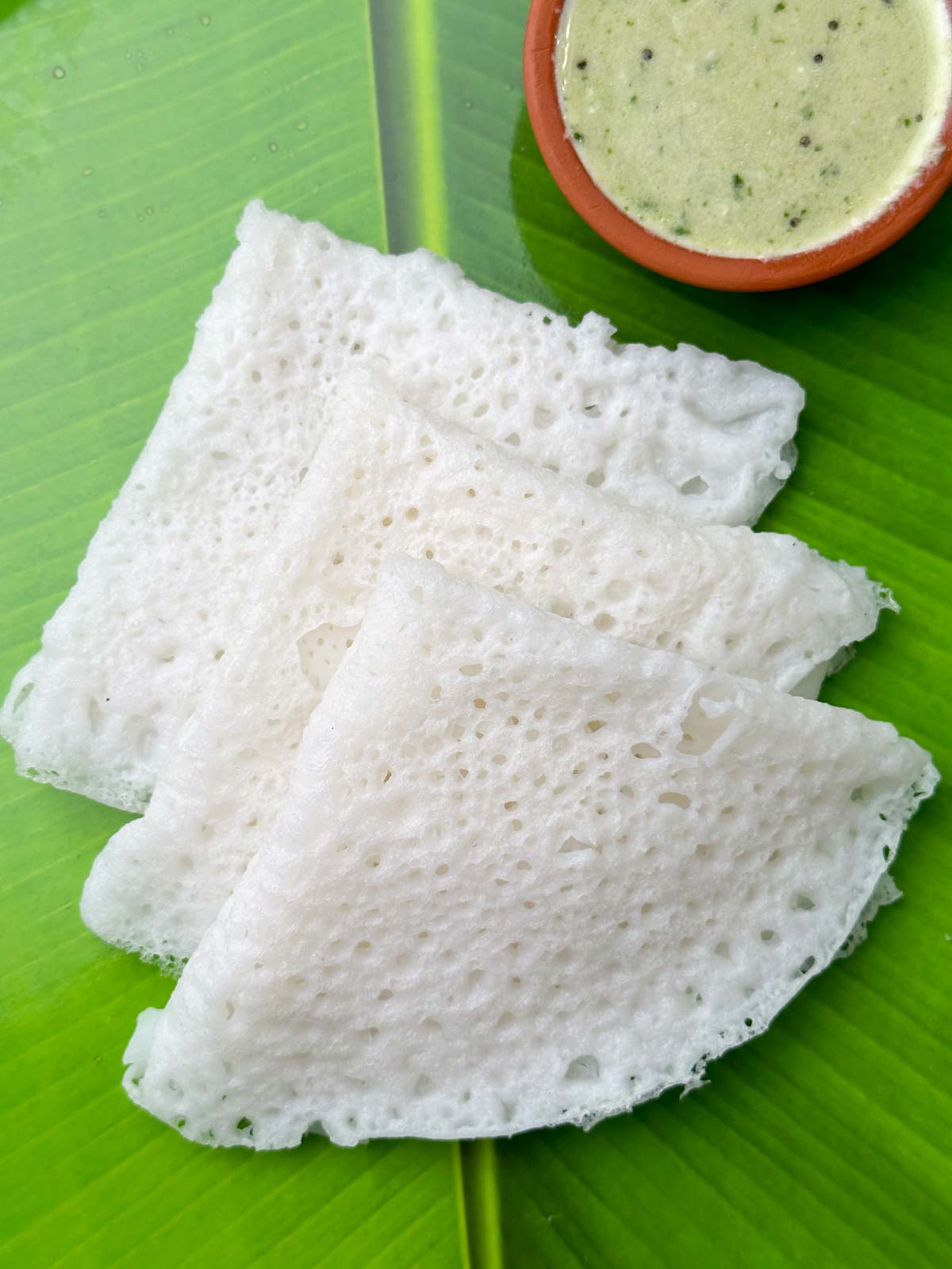 three neer dosa layed on each other with coconut chutney on the side