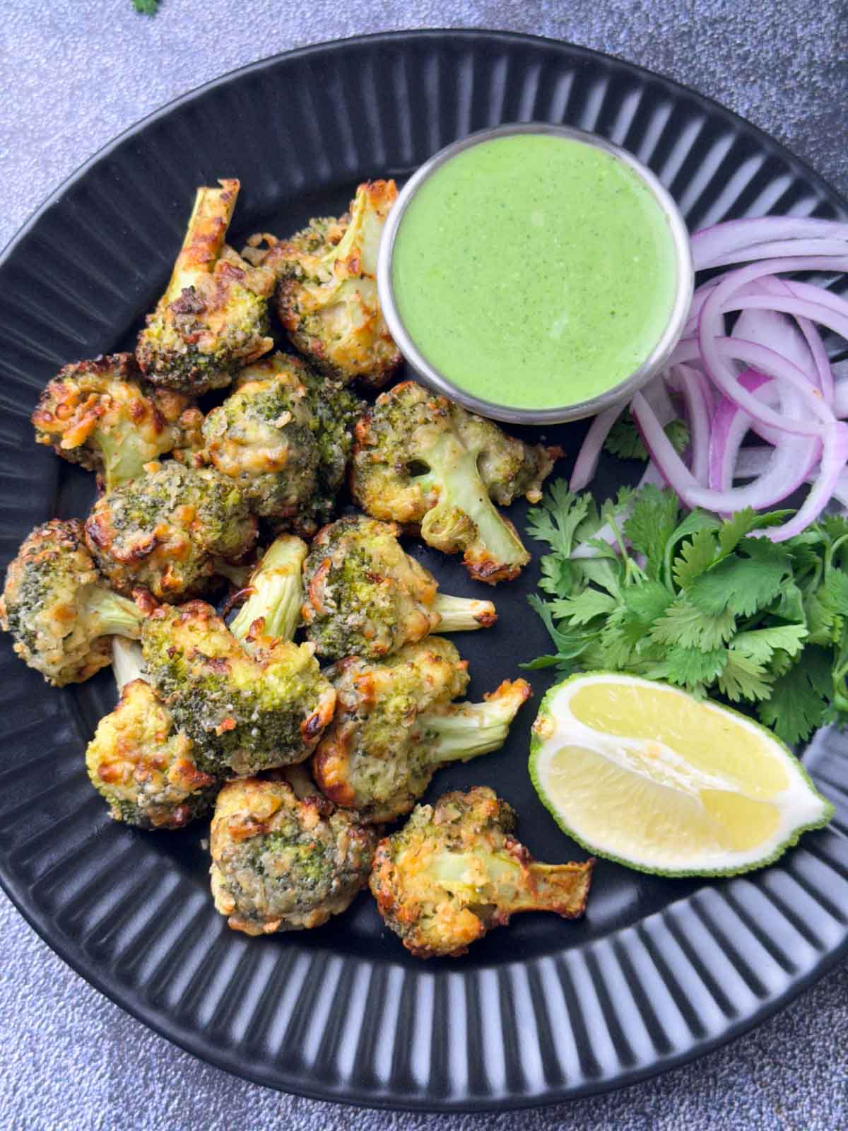 tandoori malai broccoli served on a plate with mint yogurt chutney, onions and lime wedge