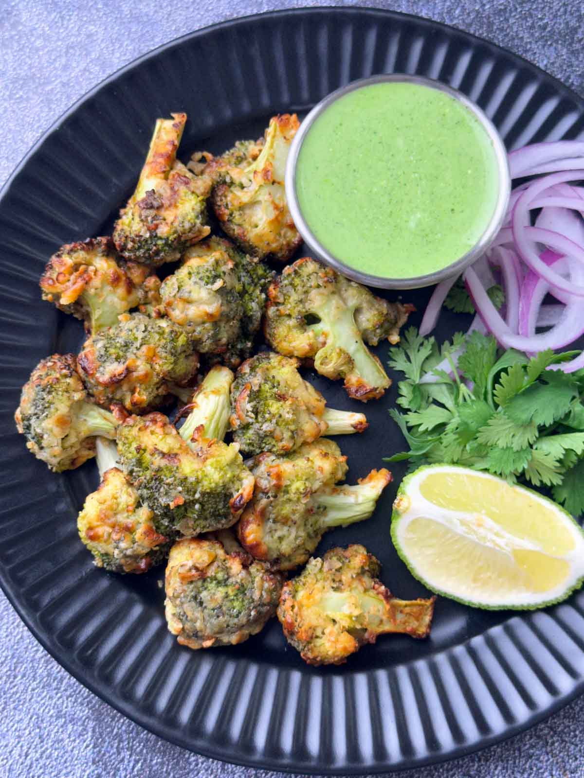 tandoori malai broccoli served on a plate with mint yogurt chutney, onions and lime wedge