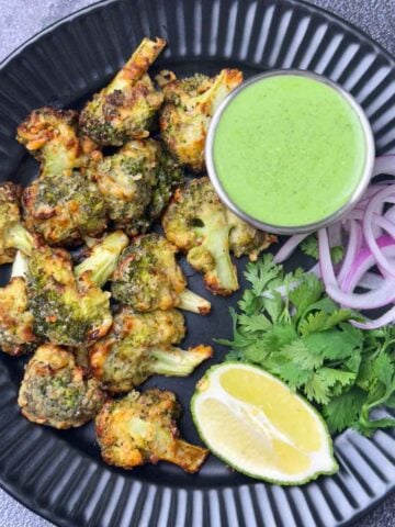 tandoori malai broccoli tikka served on a plate with mint yogurt chutney, onions and lime wedge