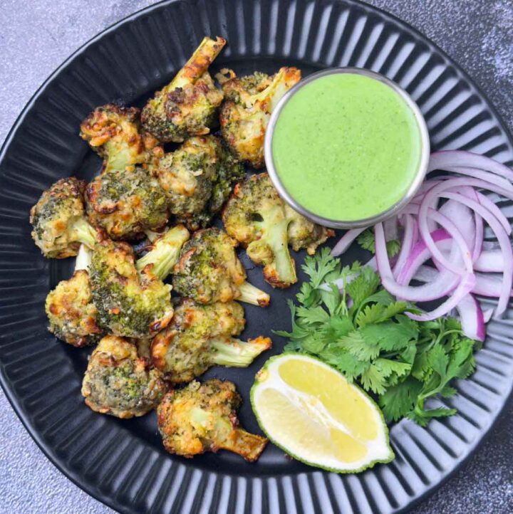 tandoori malai broccoli tikka served on a plate with mint yogurt chutney, onions and lime wedge