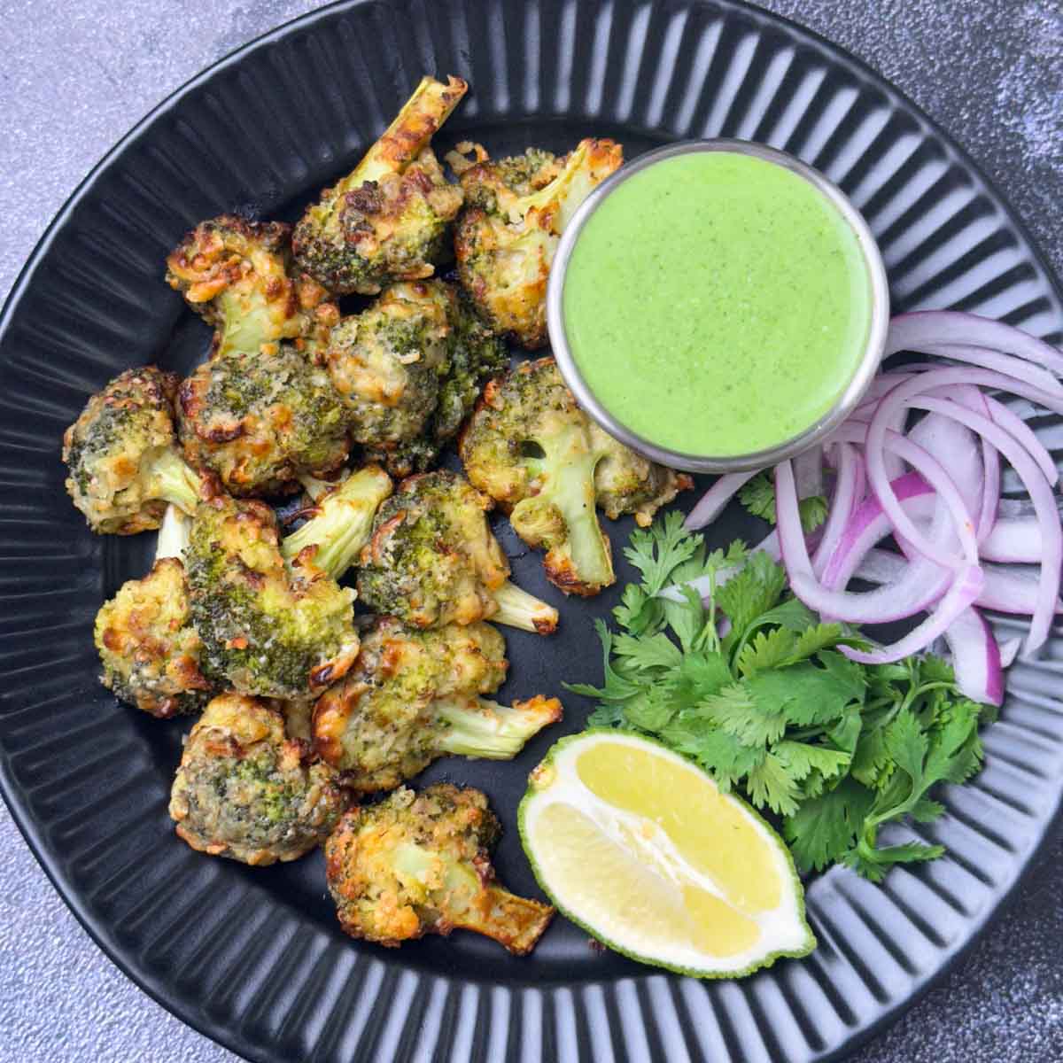 tandoori malai broccoli tikka served on a plate with mint yogurt chutney, onions and lime wedge