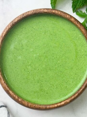 Mint yogurt chutney served in a bowl with herbs on the side