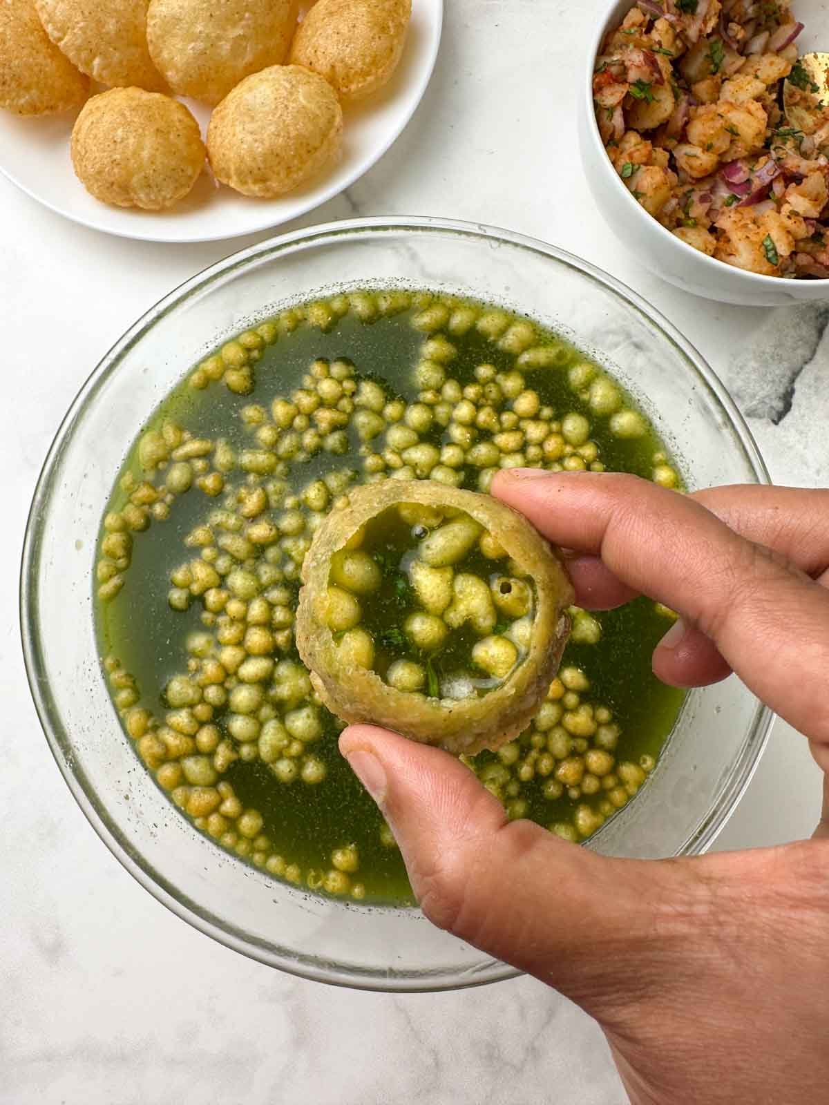 pani puri (golgappa) in hand with puri and potato mixture on the side