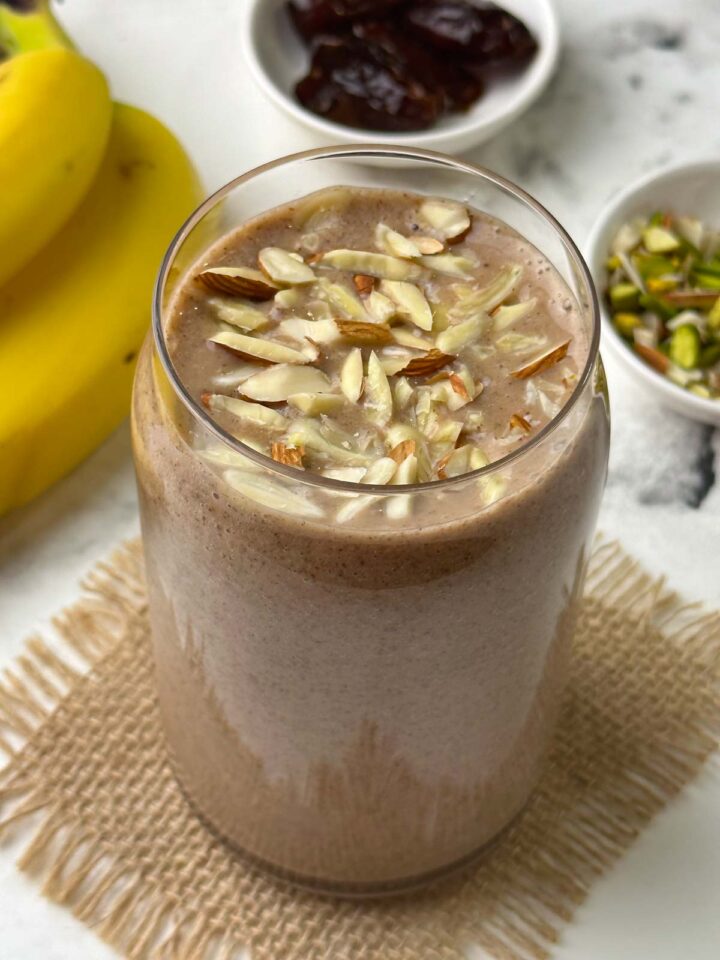 ragi banana dates smoothie served in a glass topped with almonds with banana, dates and nuts on the side