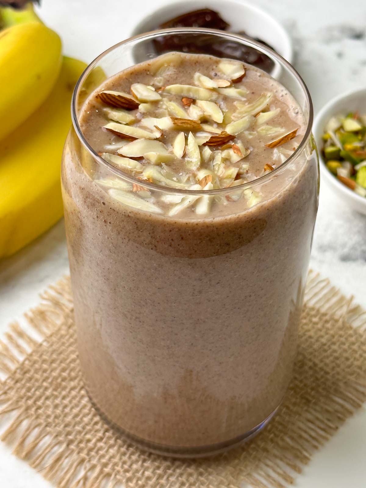 ragi banana dates smoothie served in a glass topped with almonds with banana, dates and nuts on the side