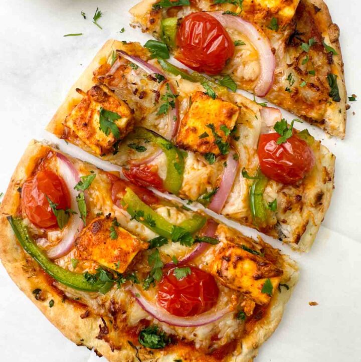 tandoori paneer naan pizza served on a sheet with coriander leaves on the side