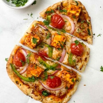 tandoori paneer naan pizza served on a sheet with coriander leaves on the side