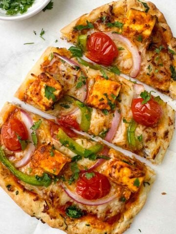 tandoori paneer naan pizza served on a sheet with coriander leaves on the side