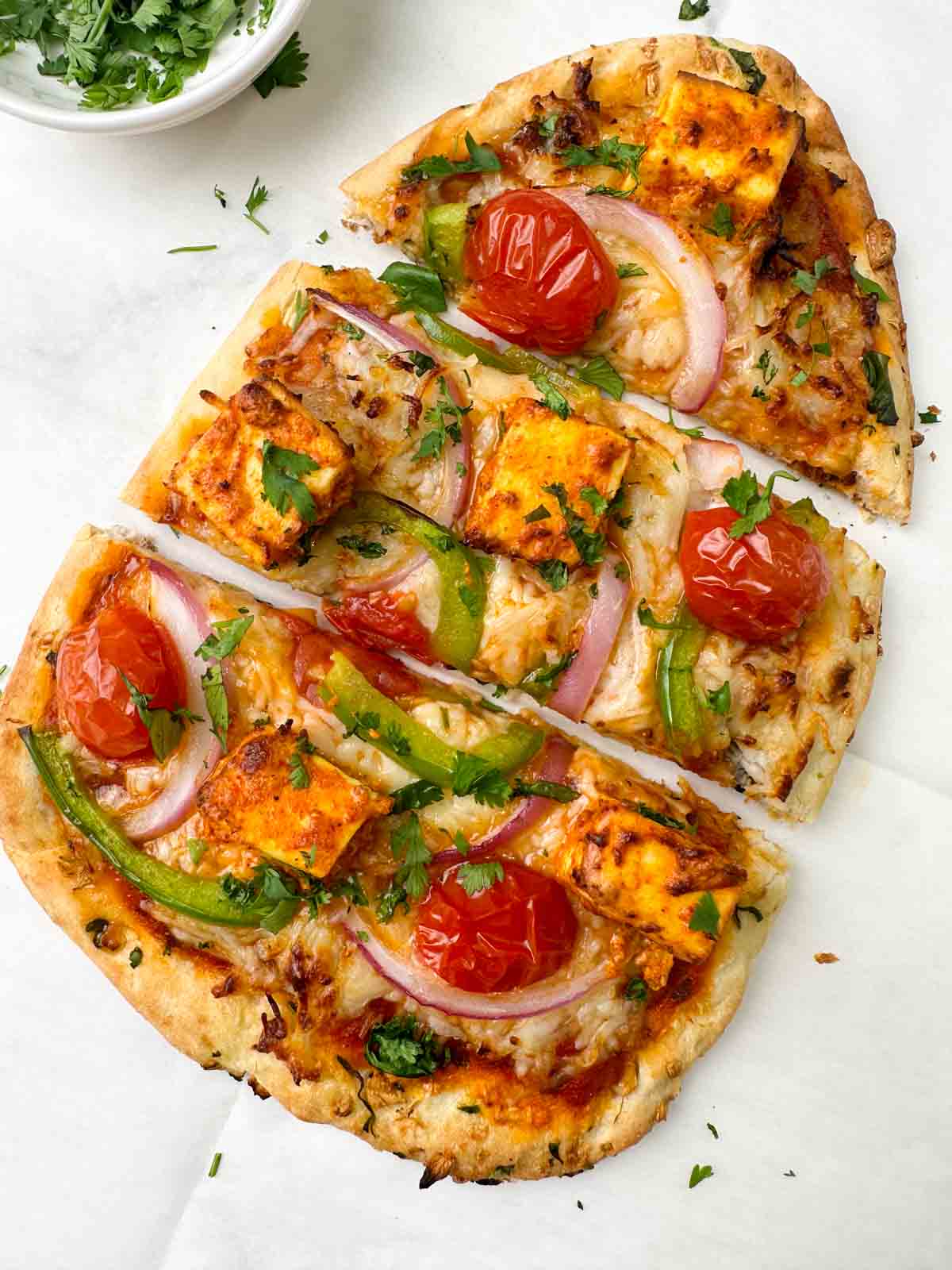 tandoori paneer naan pizza served on a sheet with coriander leaves on the side