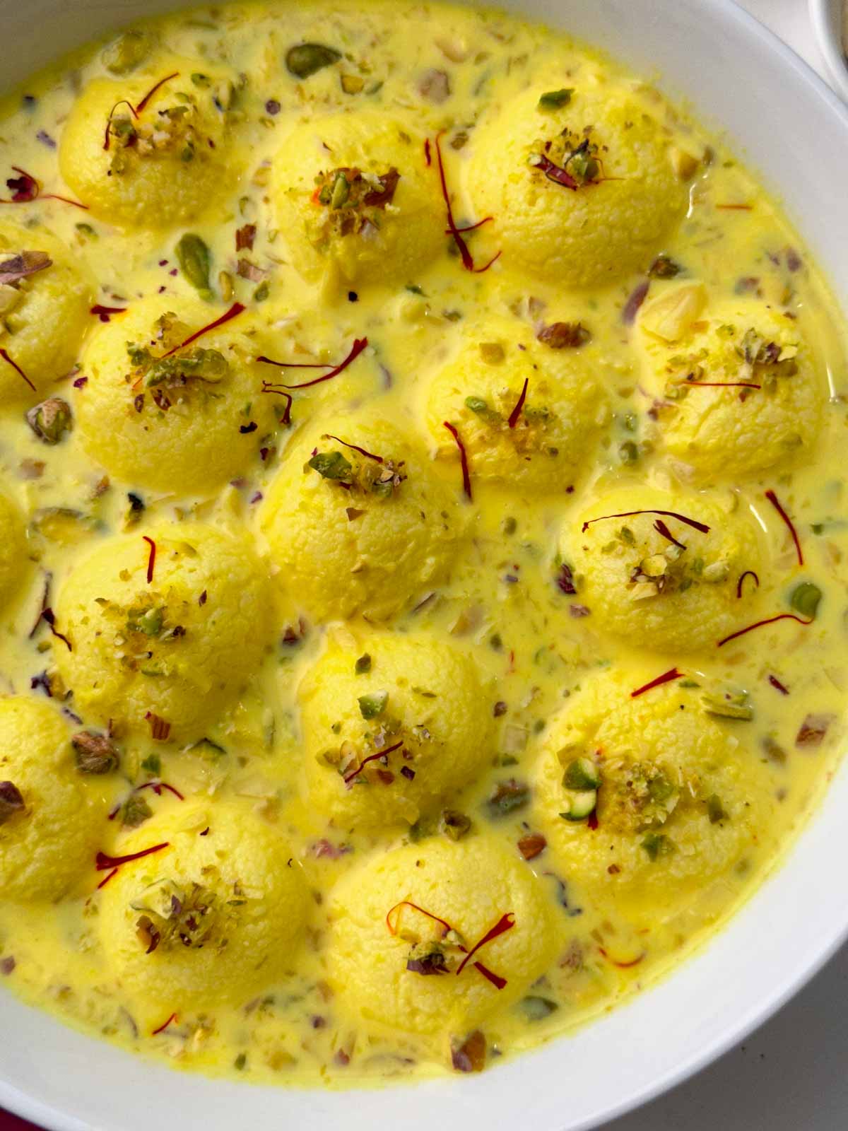 Easy rasmalai recipe in a serving bowl garnished with nuts and saffron