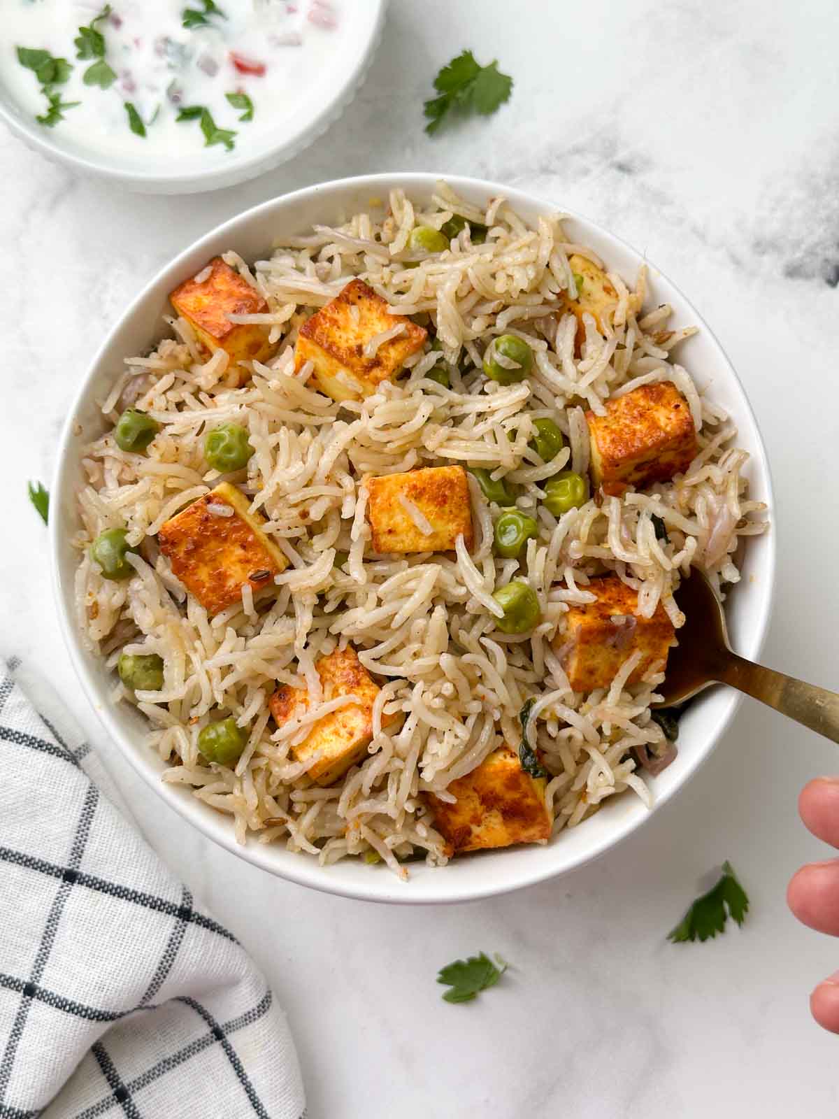 paneer peas pulav in a bowl with a spoon and raita on the side