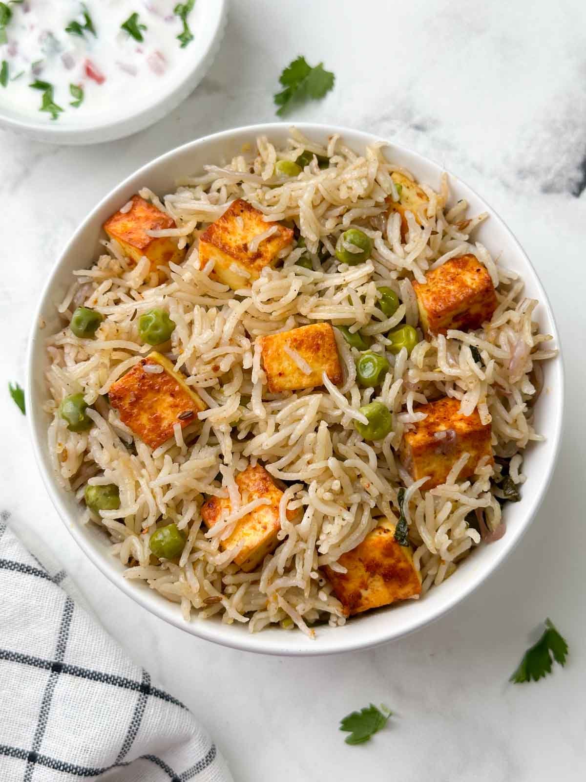 peaneer matar pulao served n a bowl with raita on the side