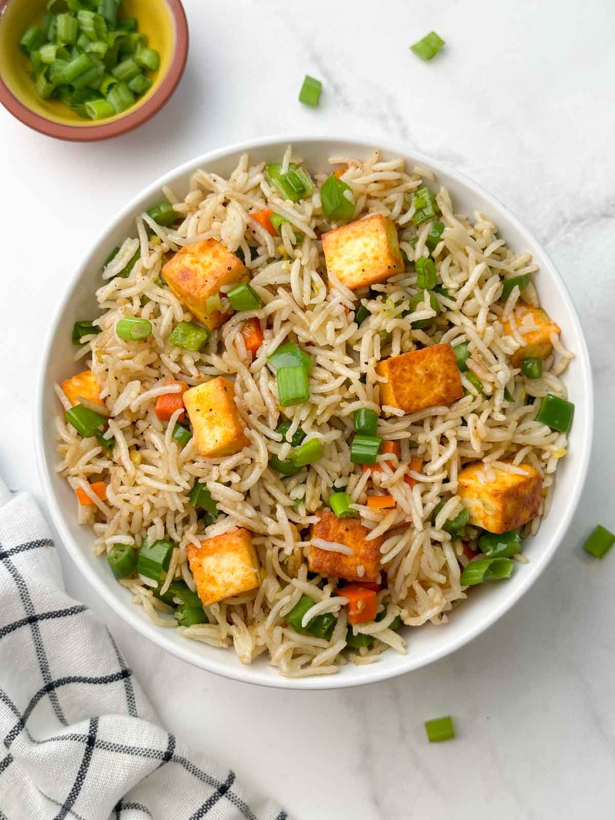 paneer vegetable fried rice in a bowl with green onions on the side