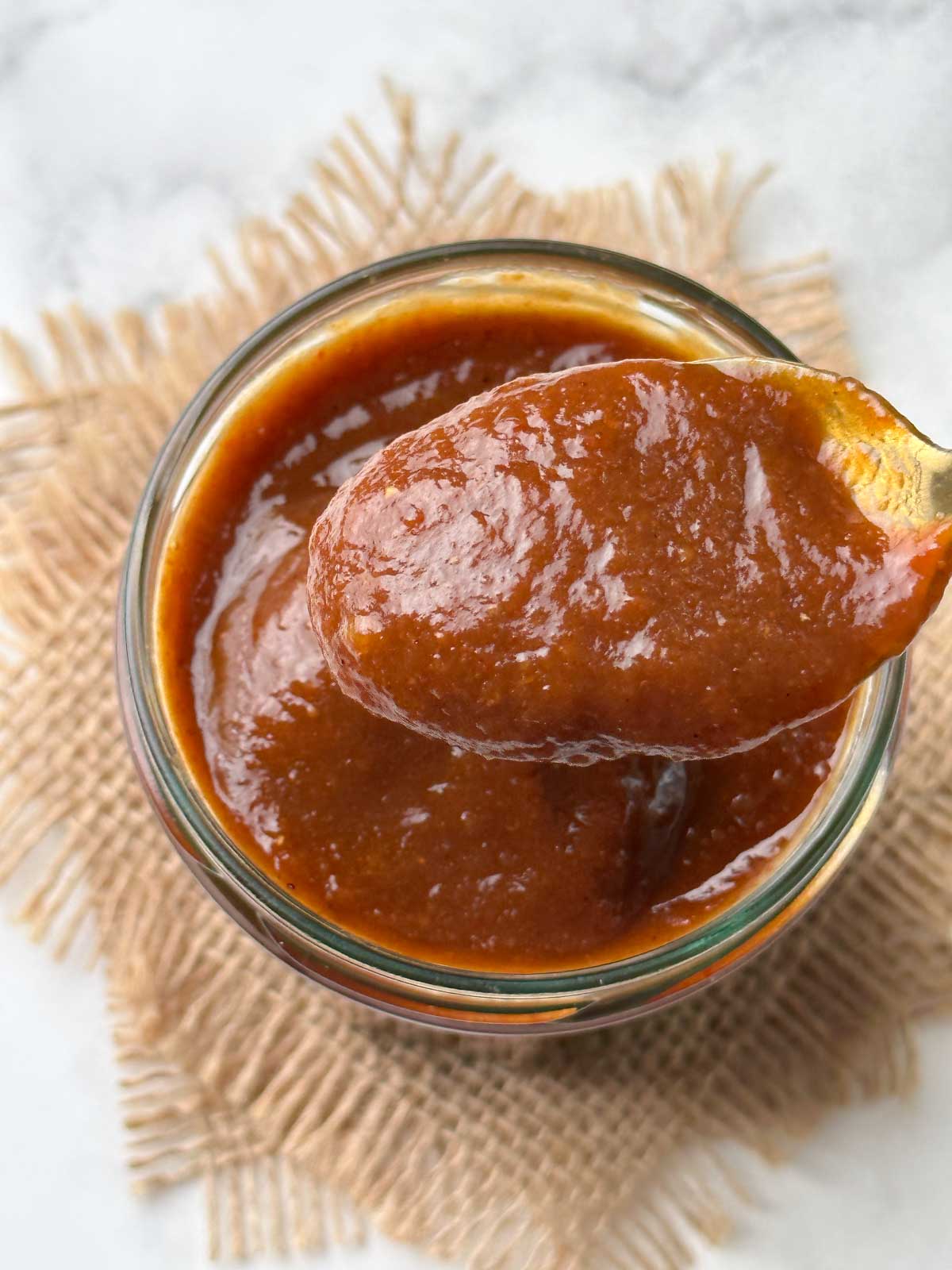 date tamarind chutney in a galss container with spoon full of chutney