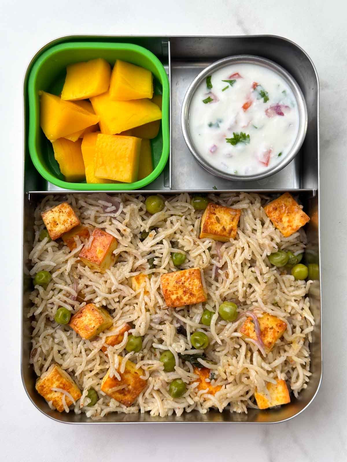 Paneer pulao with raita and mango fruit in bento steel box