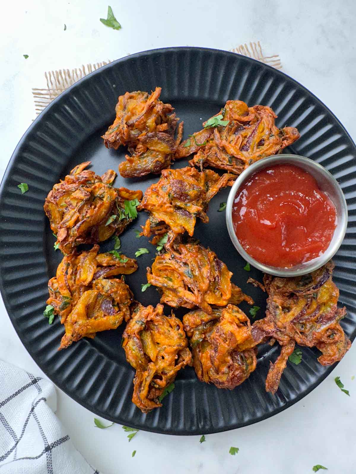 deep fried onion pakoda on a black plate with ketchup on the side