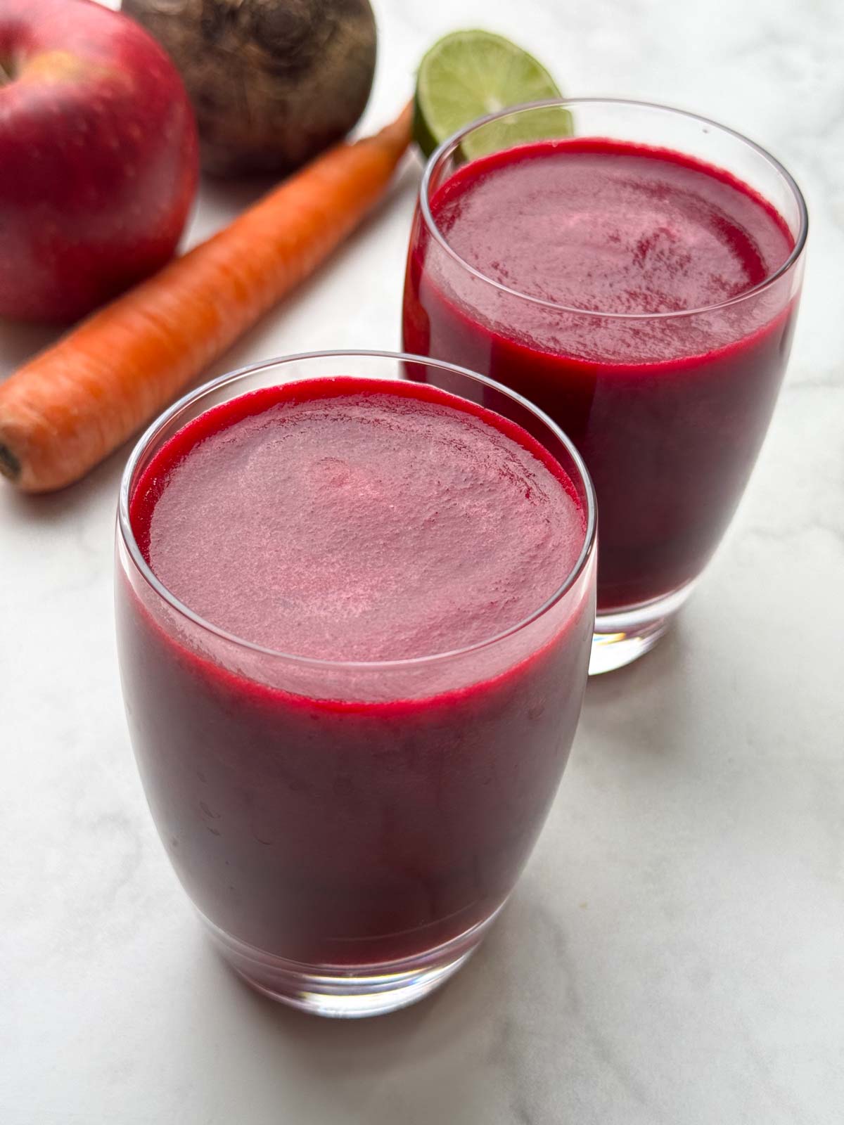 ABC juice served in 2 glasses with beets, apple and carrots on the side