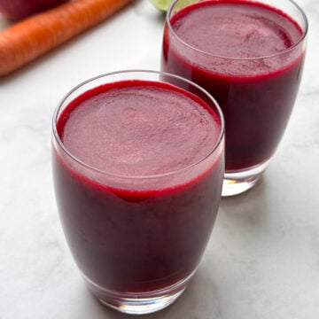 apple beetroot carrot juice served in 2 glasses with beets, apple and carrots on the side