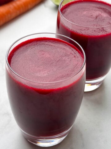 apple beetroot carrot juice served in 2 glasses with beets, apple and carrots on the side