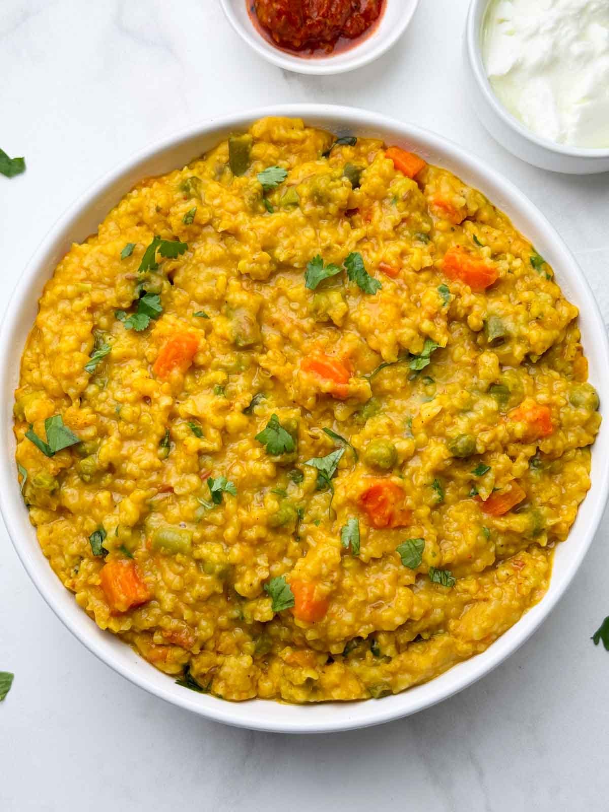 vegetable dalia khichdi (broken wheat khichdi) served in a bowl with pickle and yogurt on the side