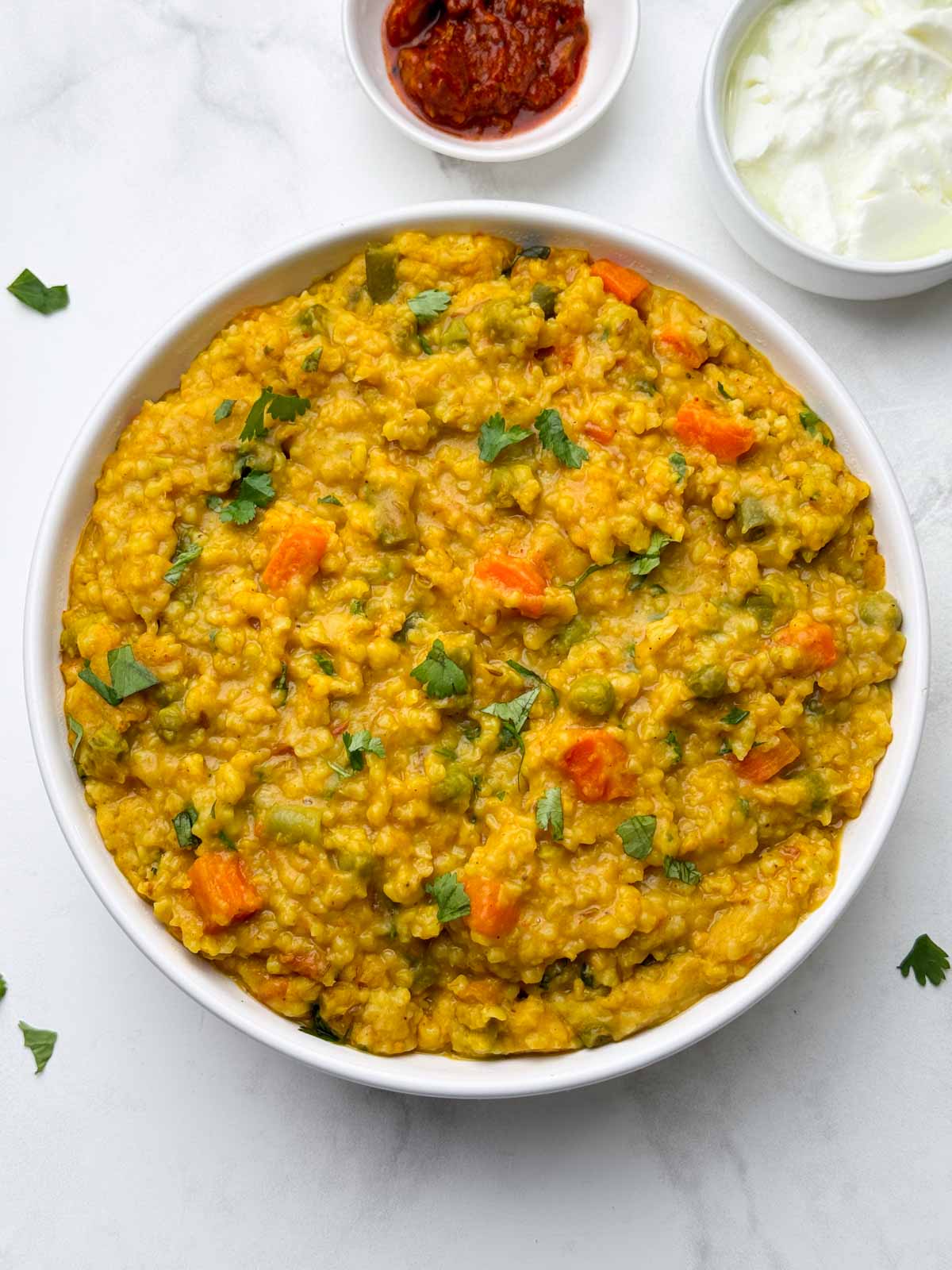 vegetable dalia khichdi (broken wheat khichdi) served in a bowl with pickle and yogurt on the side