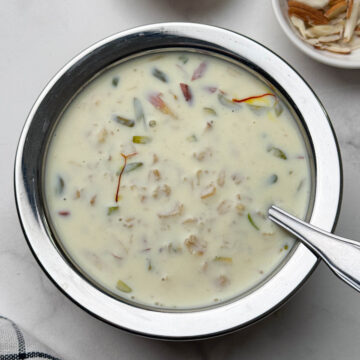 oats kheer served in a steel bowl with a spoon and nuts on the side