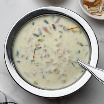 oats kheer served in a steel bowl with a spoon and nuts on the side