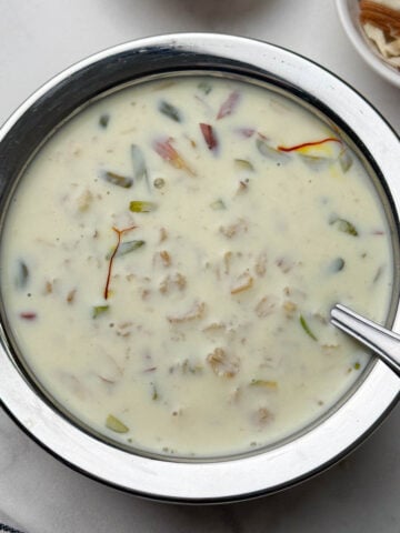 oats kheer served in a steel bowl with a spoon and nuts on the side