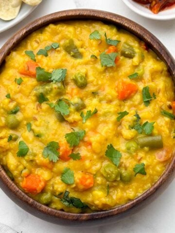 vegetable oats khichdi served in a bowl with papd and pickle on the side