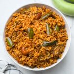 vangi bhath rice served in a bowl with green brinjals on the side